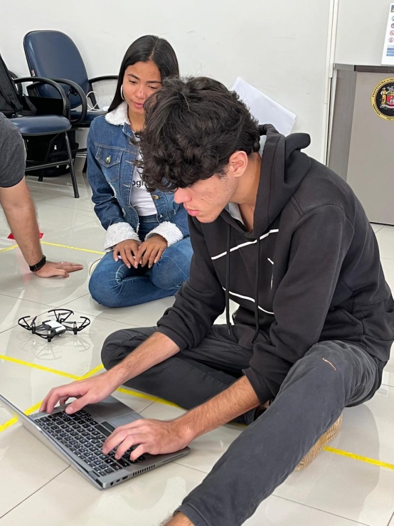 A student sits on the floor working on a laptop during the course, with two others next to him.