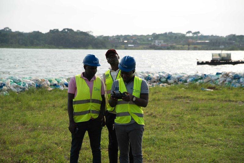 Team members of Uganda Flying Labs stand with Lake Victoria in the background. They are wearing reflector jackets and observing a drone flight.