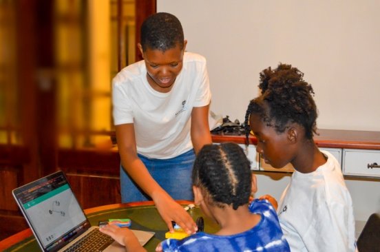 A trainer from Botswana Flying Labs smiles as she guides young workshop participants working on a laptop.