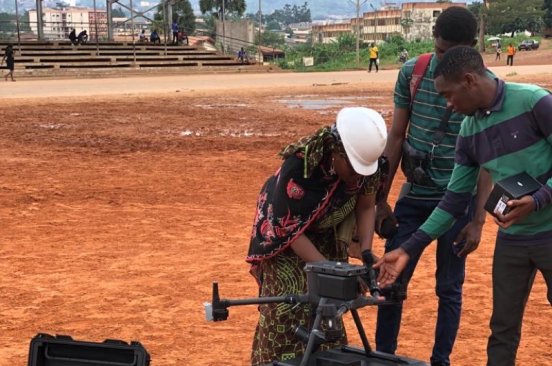 Team members from Cameroon Flying Labs set up a drone in a dusty field for a drone training session with MINDCAF personnel.