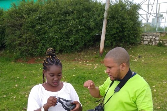 Two team members of Haiti Flying Labs stand outside in a grassy area discussing something.