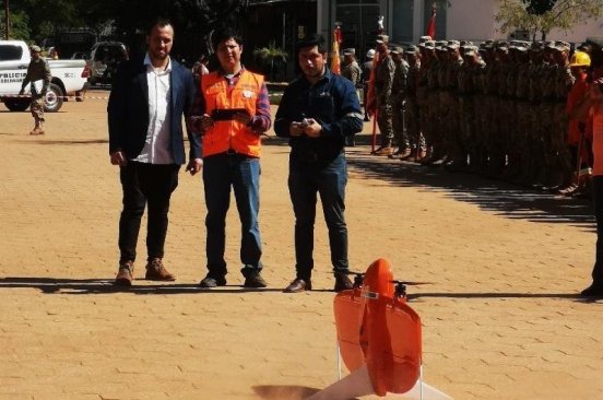 Bolivia Flying Labs and two representatives from Wingtra demonstrate a flight using a bright orange Wingtra drone in the foreground.