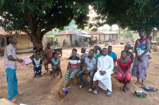 Local community members sit under trees listening to a team member from Benin Flying Labs