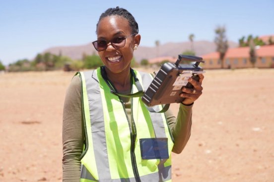 A drone pilot from Namibia Flying Labs holds a controller while smiling at the camera.