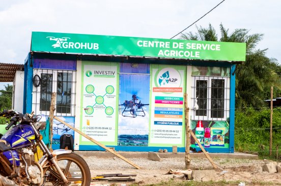 A photograph of an agrohub - a small building, the outside of which displays an image of a drone as well as information about the services offered.