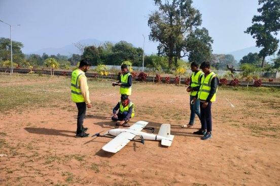 India Flying Labs team members and drone medical delivery interns stand outside around a drone.