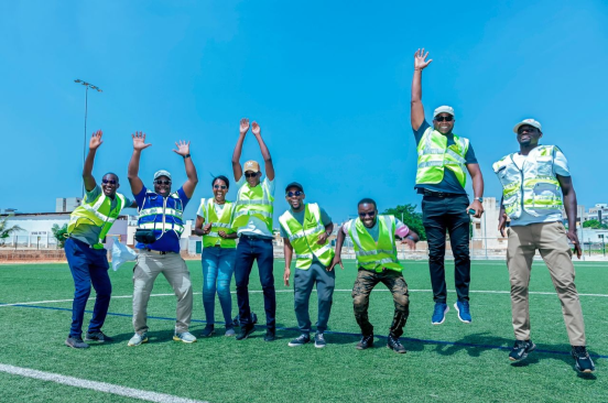 A group photo of the Senegal Flying Labs team in a field, wearing reflector vests, jumping excitedly.