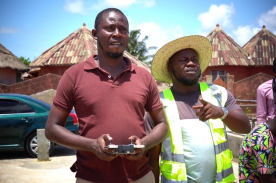 A man concentrates as he flies a drone in Benin. Next to him is a man in a reflector vest.